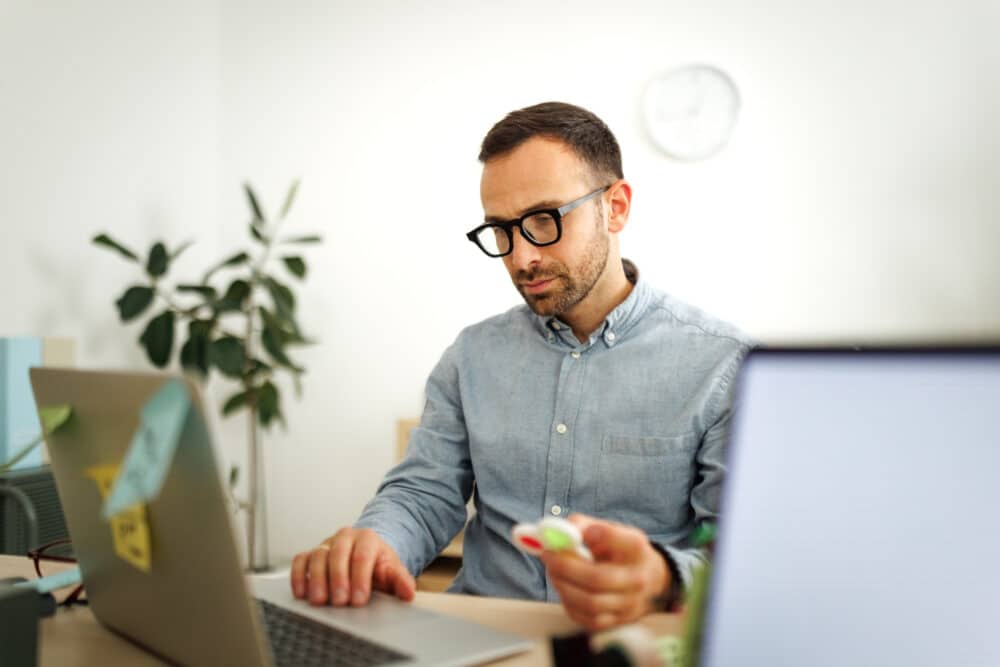 Young well dressed businessman working at office, using fidget spinner for stress relief
